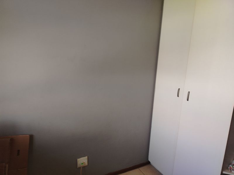 A bedroom interior featuring a neutral grey wall and a white built-in wardrobe with modern handles.