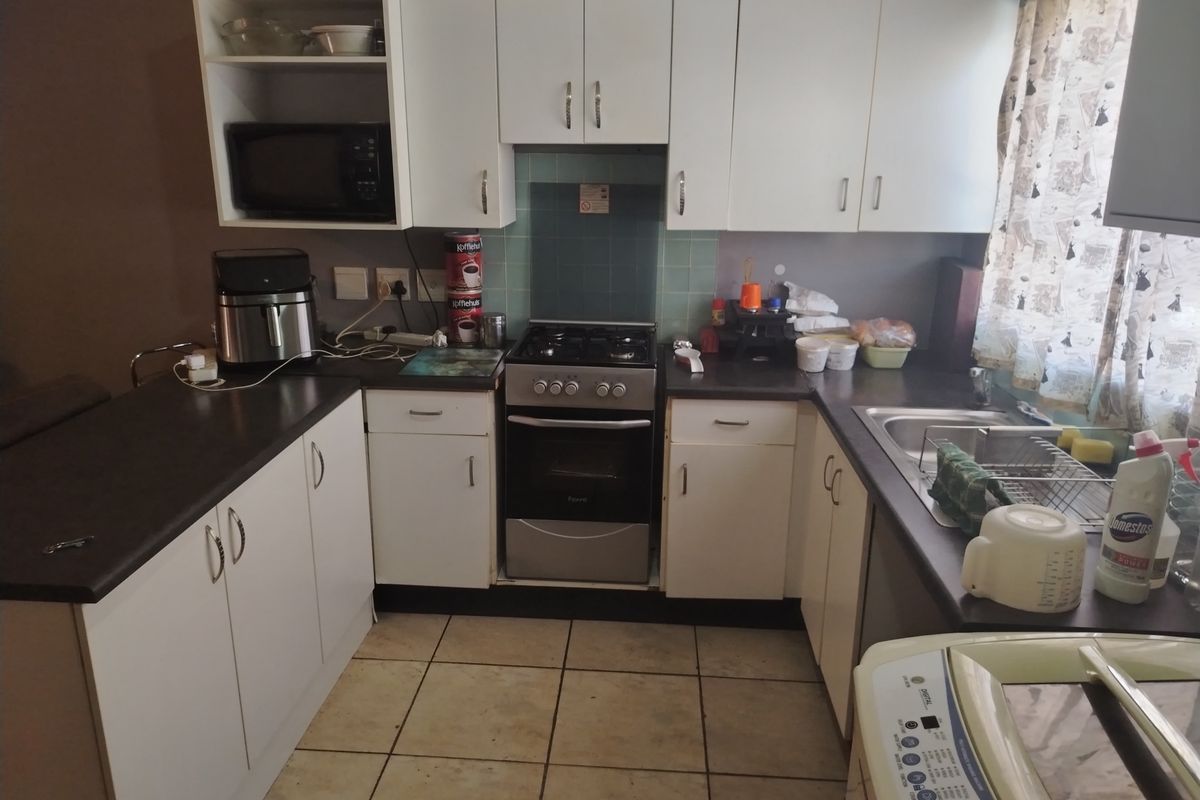 Functional kitchen featuring white built-in cabinetry, gas stove with oven, stainless steel sink, and tiled flooring, offering a practical layout for daily use.