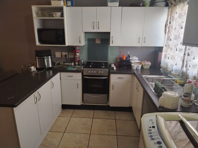 Functional kitchen featuring white built-in cabinetry, gas stove with oven, stainless steel sink, and tiled flooring, offering a practical layout for daily use.