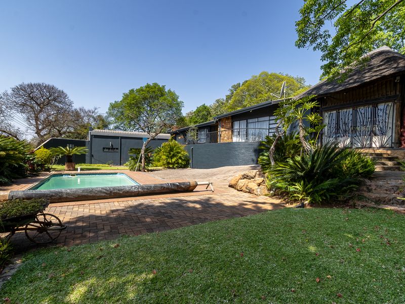 Rear exterior view featuring a swimming pool, landscaped garden, brick paved patio area, and a house with a thatched roof section.
