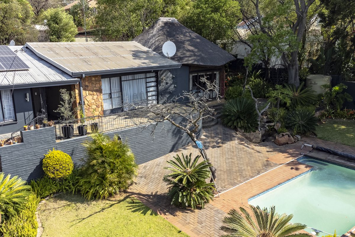 Aerial view of the rear exterior featuring a swimming pool, paved patio area, thatched roof section, and solar panels on the main roof.