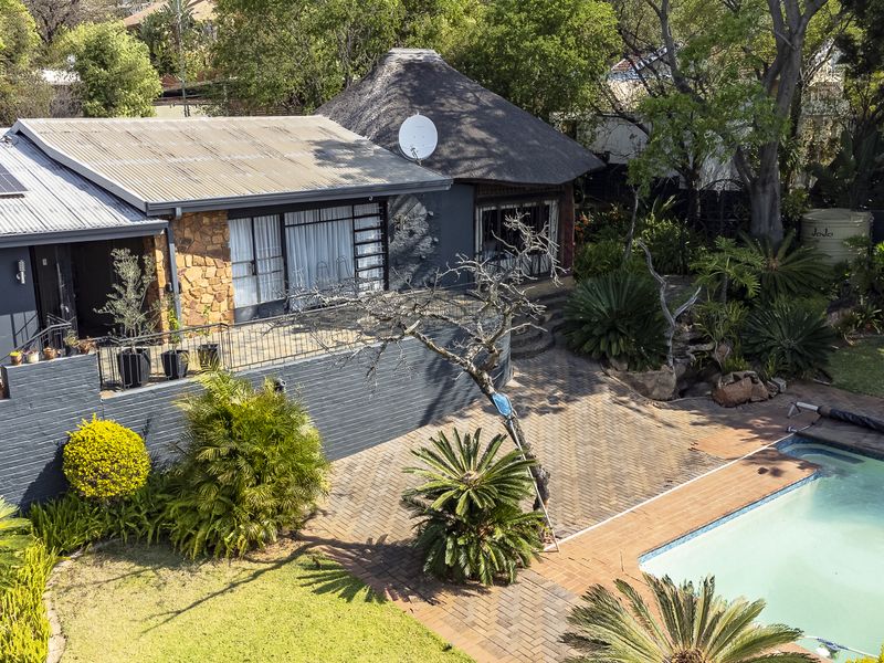 Aerial view of the rear exterior featuring a swimming pool, paved patio area, thatched roof section, and solar panels on the main roof.