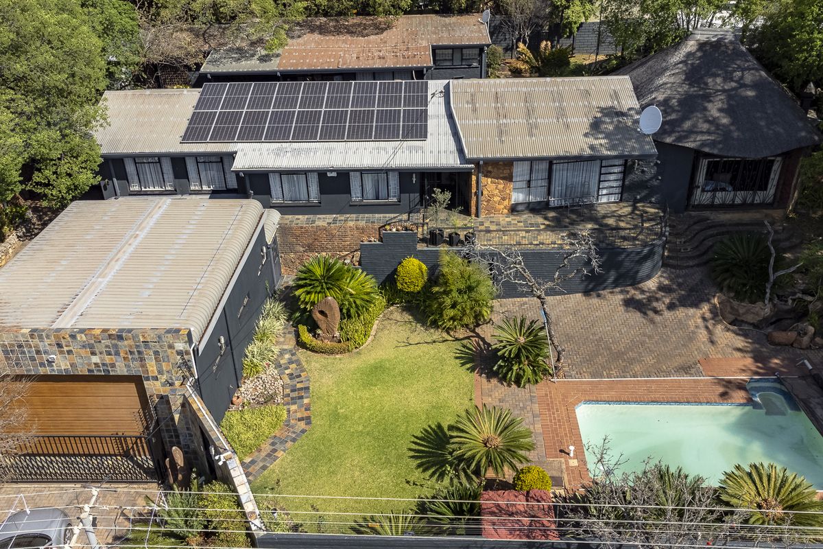 Aerial view of a residential property featuring a swimming pool, solar panel installation, paved outdoor areas, and a mix of modern and traditional roof styles.