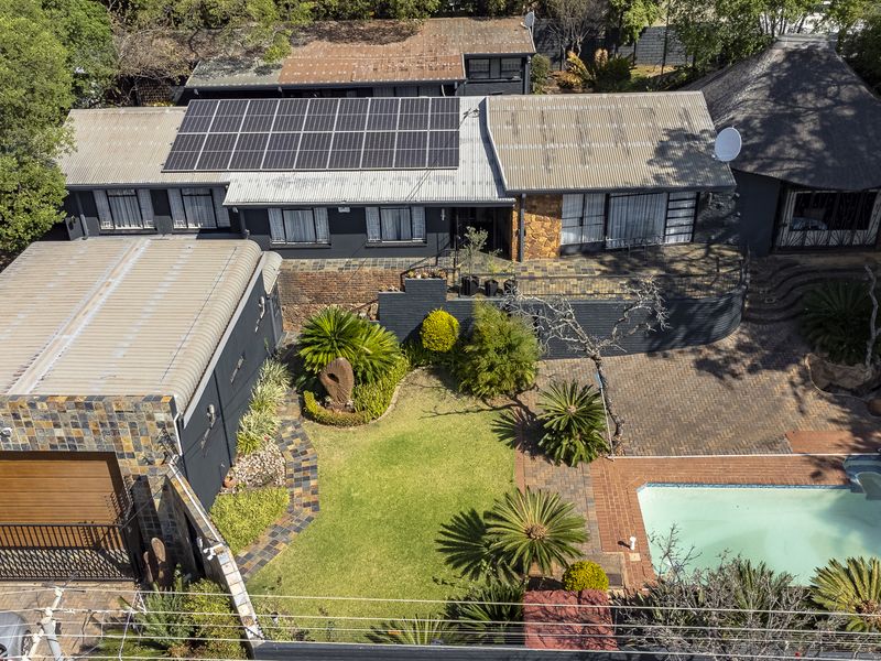 Aerial view of a residential property featuring a swimming pool, solar panel installation, paved outdoor areas, and a mix of modern and traditional roof styles.