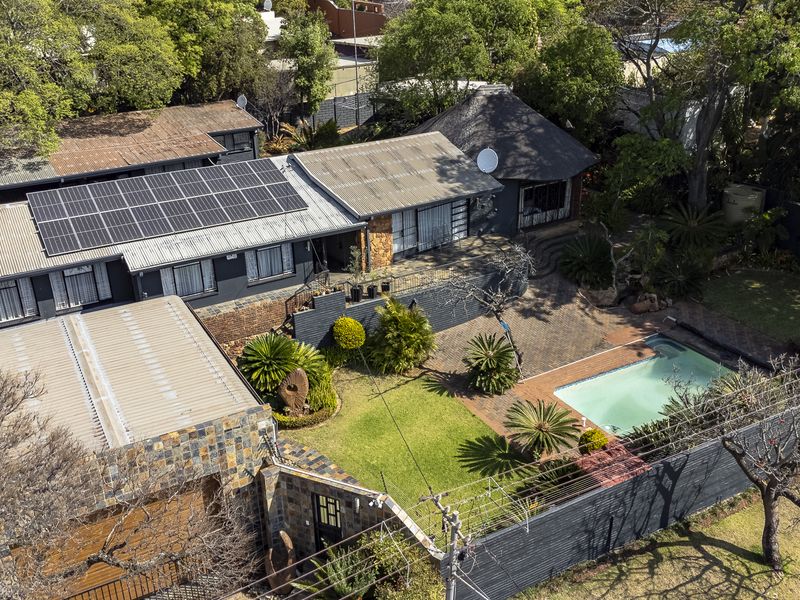 Aerial view of a residential property featuring a swimming pool, landscaped garden, paved patio, and solar panel installation on the roof.
