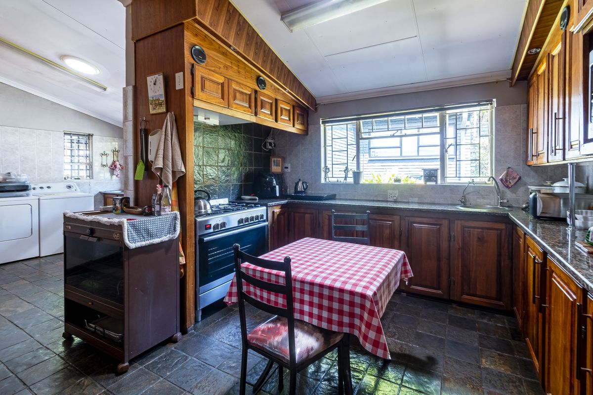 A functional kitchen featuring wooden cabinetry, a gas stove with extractor, and an adjacent laundry area with tiled flooring throughout.
