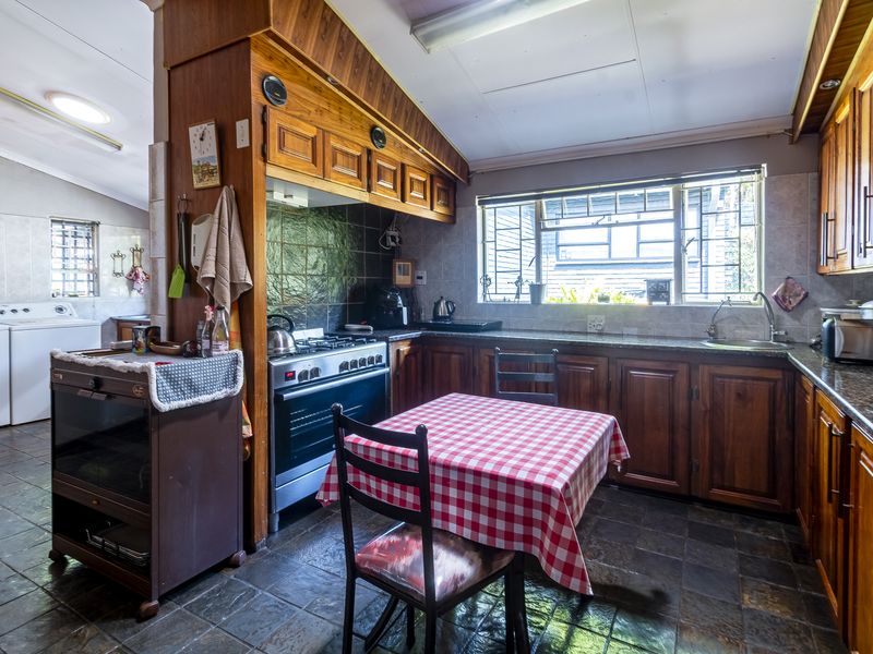 A functional kitchen featuring wooden cabinetry, a gas stove with extractor, and an adjacent laundry area with tiled flooring throughout.