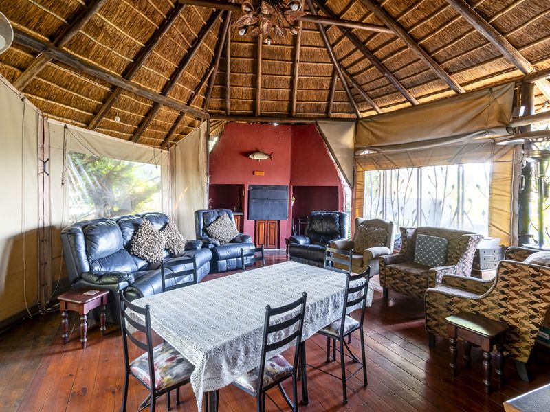 A rustic living and dining area featuring a traditional thatched roof, exposed timber rafters, timber flooring, and a built-in fireplace.