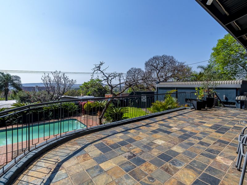 Spacious elevated patio featuring slate tile flooring and wrought iron railings, overlooking the swimming pool and garden area.