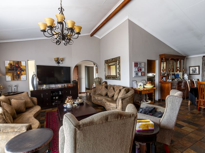 Spacious open-plan living and dining area featuring vaulted ceilings with exposed timber beams, slate tile flooring, and a classic wrought iron chandelier.