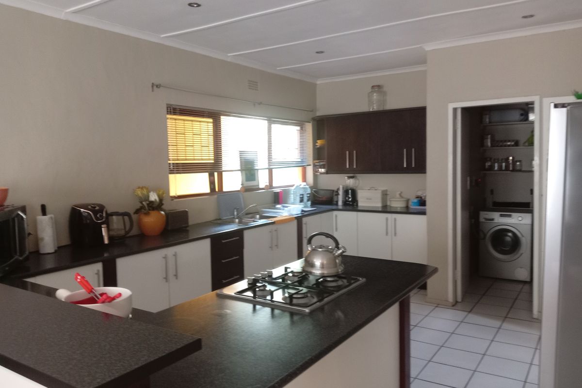 Functional kitchen featuring dark cabinetry, contrasting countertops, a gas hob, and tiled flooring, with an adjacent scullery area visible.