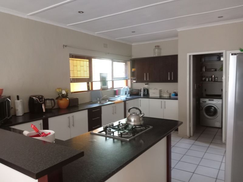 Functional kitchen featuring dark cabinetry, contrasting countertops, a gas hob, and tiled flooring, with an adjacent scullery area visible.