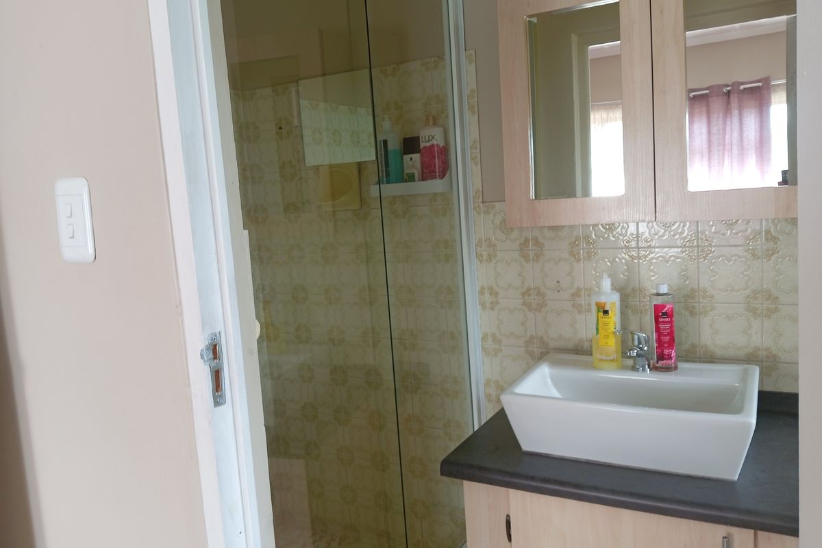 A functional bathroom featuring a glass-enclosed shower, a modern vessel sink set on a vanity cabinet, and decorative wall tiling.