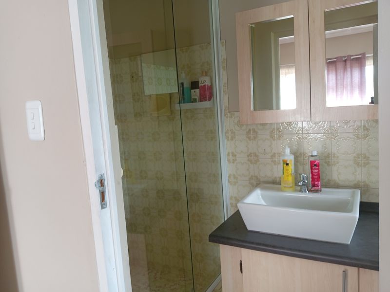 A functional bathroom featuring a glass-enclosed shower, a modern vessel sink set on a vanity cabinet, and decorative wall tiling.