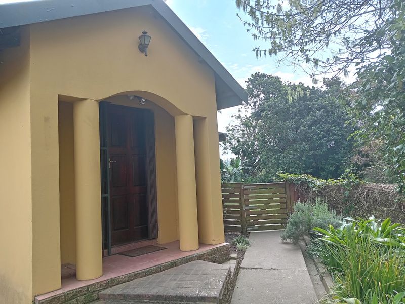 Front entrance of the small holding featuring a covered porch with decorative columns, a concrete walkway, and a wooden garden gate.