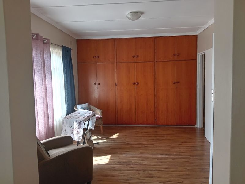 A bedroom featuring extensive floor-to-ceiling wooden built-in cupboards and laminate flooring, offering ample storage space.