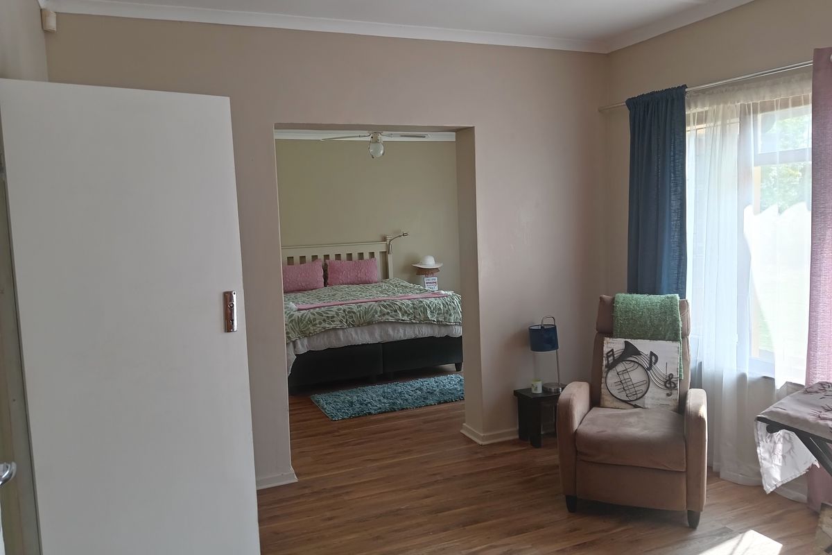 A bedroom featuring laminate flooring, coved cornicing, and a ceiling fan, with an open transition to an adjoining sleeping area.