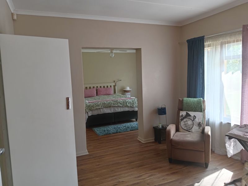 A bedroom featuring laminate flooring, coved cornicing, and a ceiling fan, with an open transition to an adjoining sleeping area.