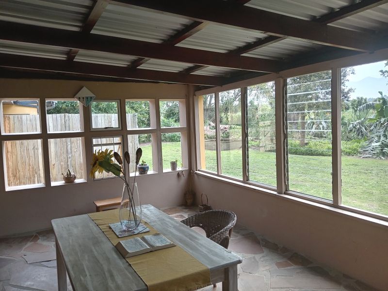 A covered patio area featuring flagstone flooring, exposed timber beams, and extensive glass windows overlooking the garden.