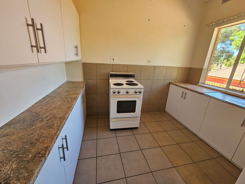 A functional kitchen featuring white cabinetry, laminate countertops, a freestanding electric stove, and tiled flooring, offering a clean and practical workspace.