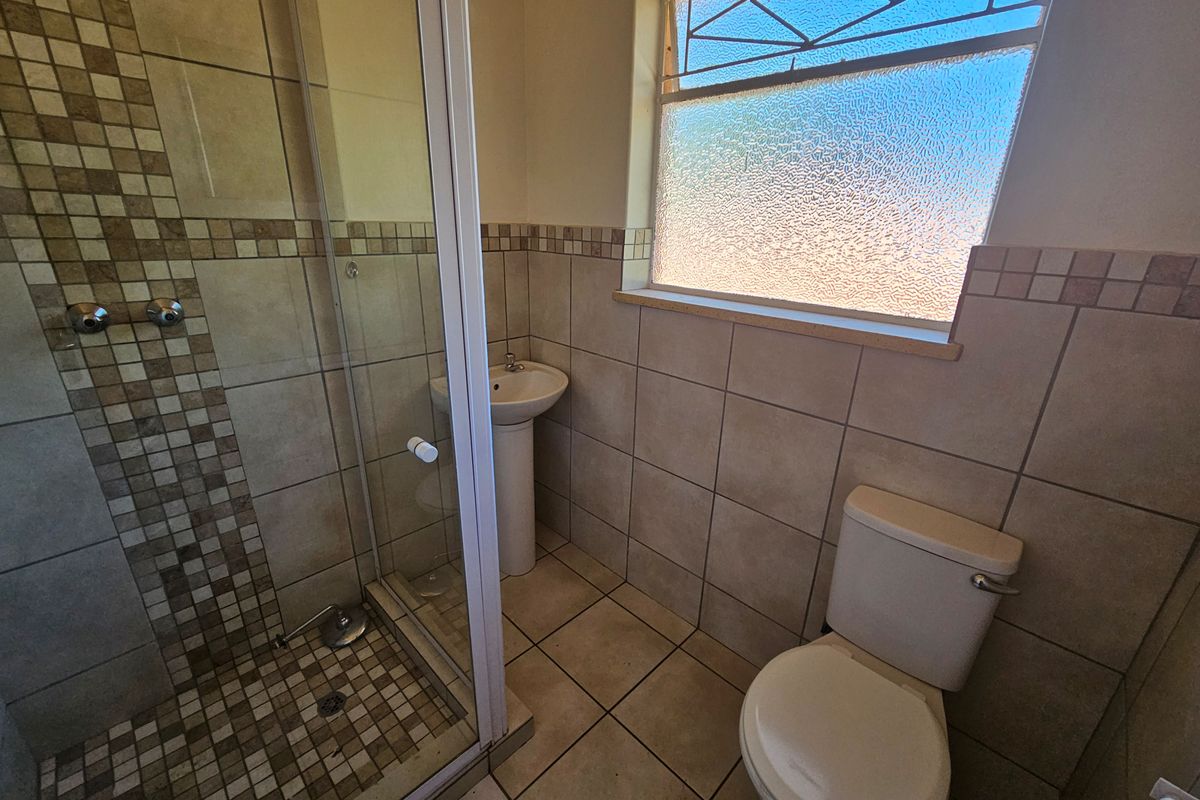 A functional bathroom featuring a shower enclosure, pedestal basin, toilet, and tiled finishes with an obscured glass window for privacy.
