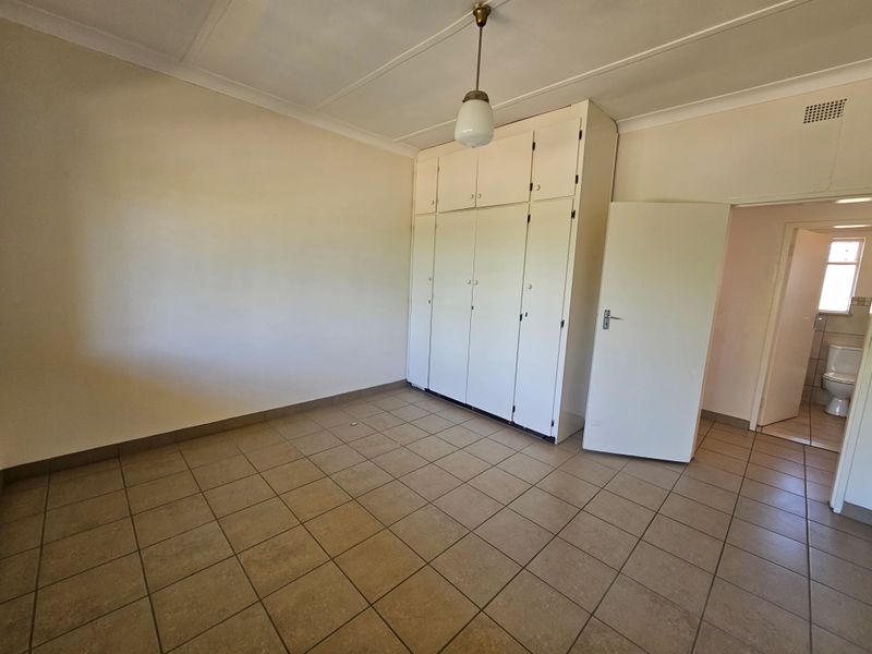A vacant bedroom featuring built-in cupboards, tiled flooring, and a coved ceiling, offering a blank canvas for personalization.