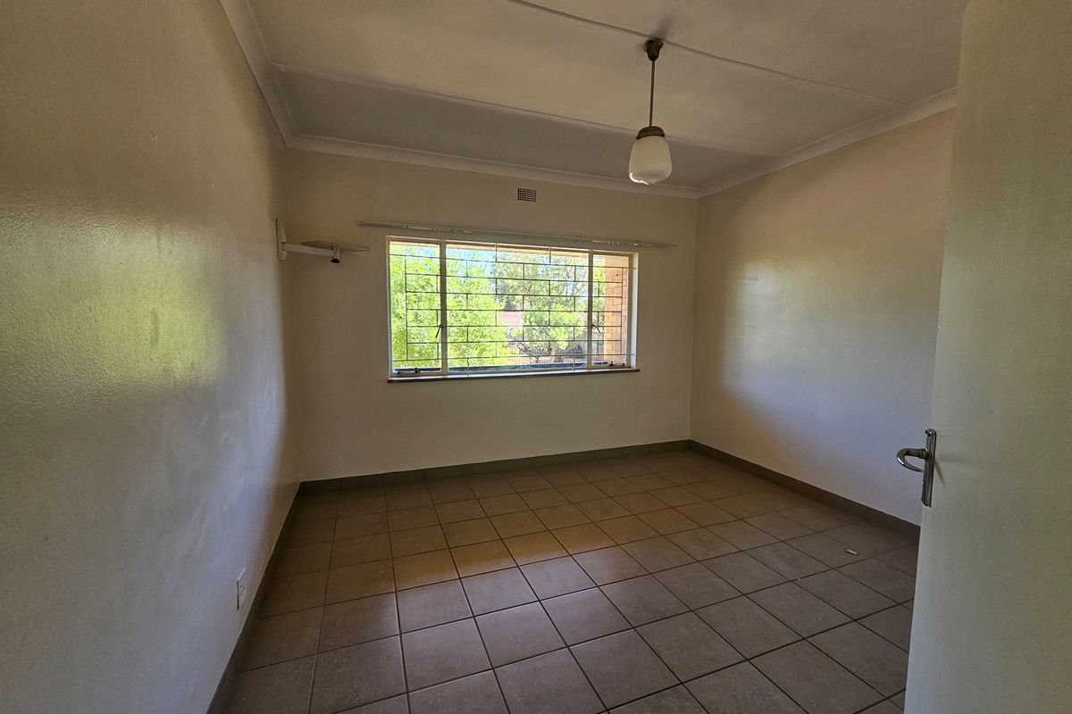 A vacant bedroom featuring tiled flooring, a large window with security bars, and a simple pendant light fixture.