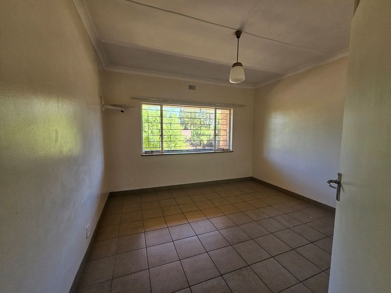 A vacant bedroom featuring tiled flooring, a large window with security bars, and a simple pendant light fixture.