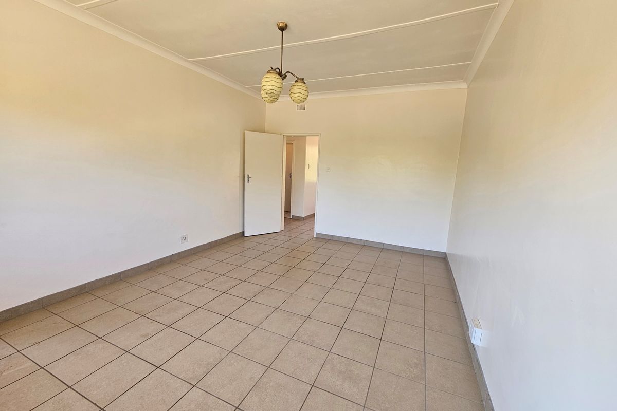 A spacious, empty living area featuring neutral tiled flooring, clean white walls, and a central pendant light fixture.
