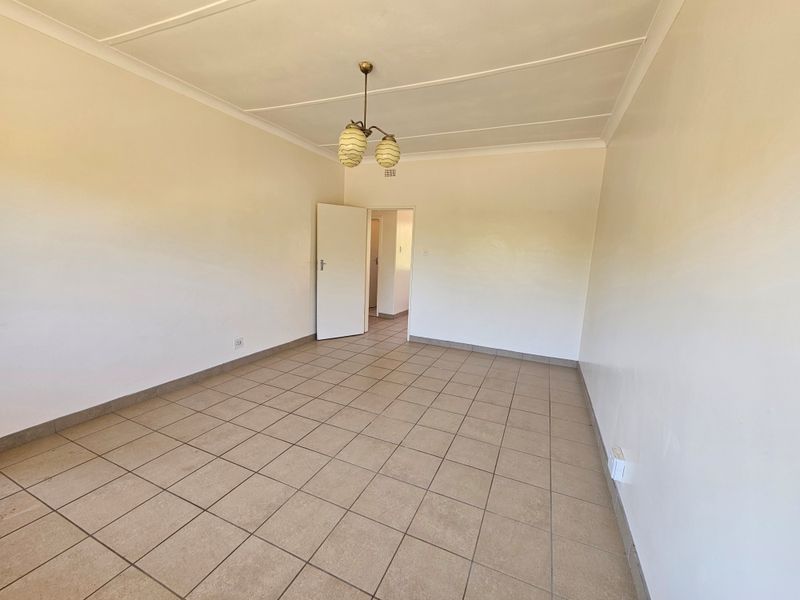A spacious, empty living area featuring neutral tiled flooring, clean white walls, and a central pendant light fixture.