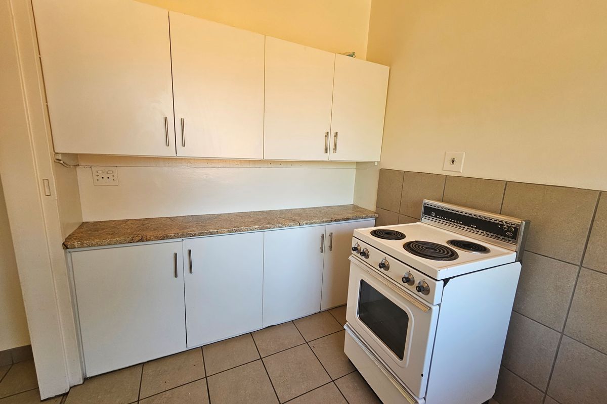 A functional kitchen area featuring white built-in cabinetry, a laminate countertop, tiled splashback, and a freestanding electric stove.