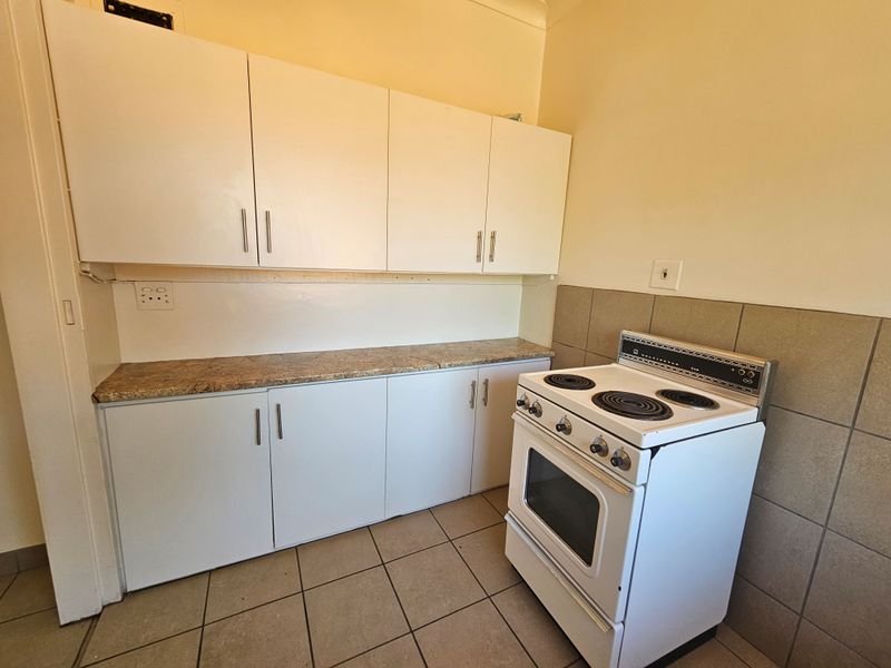 A functional kitchen area featuring white built-in cabinetry, a laminate countertop, tiled splashback, and a freestanding electric stove.