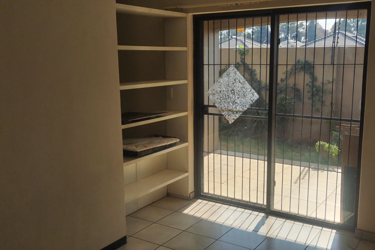 An empty living area featuring built-in shelving, tiled flooring, and a sliding glass door with a security gate leading to an outdoor patio.