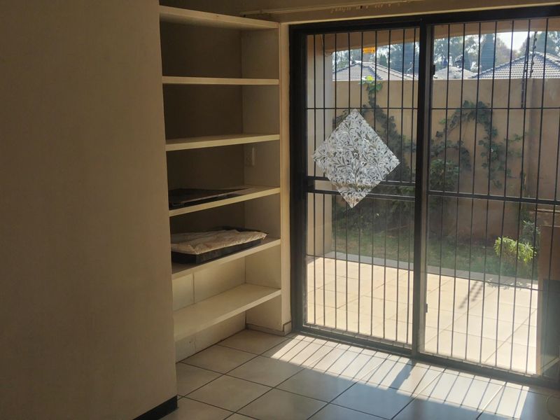 An empty living area featuring built-in shelving, tiled flooring, and a sliding glass door with a security gate leading to an outdoor patio.