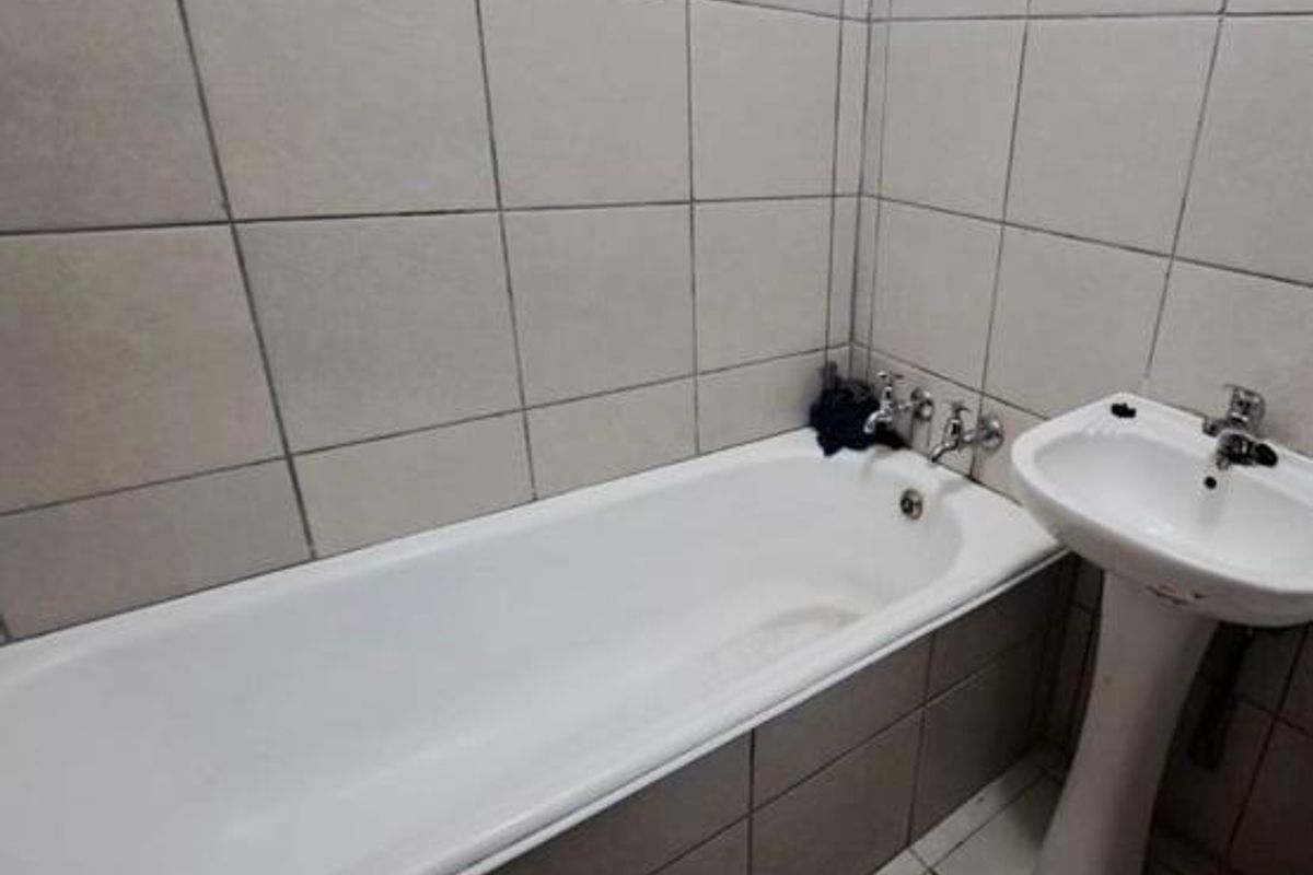 A functional bathroom featuring a standard bathtub and pedestal basin with tiled walls and flooring, requiring cosmetic updates to improve its overall condition.