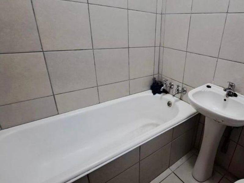 A functional bathroom featuring a standard bathtub and pedestal basin with tiled walls and flooring, requiring cosmetic updates to improve its overall condition.