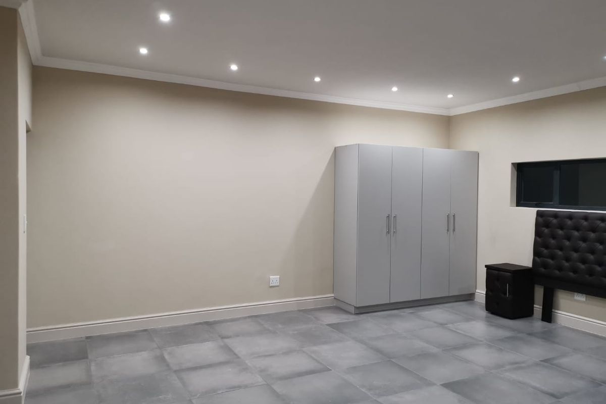 A spacious bedroom featuring modern grey tiled flooring, built-in cupboards, and recessed downlighting, offering a clean and neutral canvas for personalization.