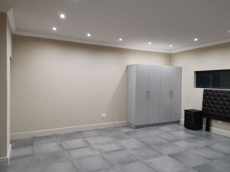 A spacious bedroom featuring modern grey tiled flooring, built-in cupboards, and recessed downlighting, offering a clean and neutral canvas for personalization.