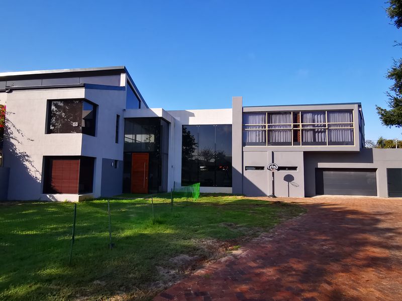 A modern architectural front elevation featuring a brick driveway, large glass windows, and a prominent entrance.