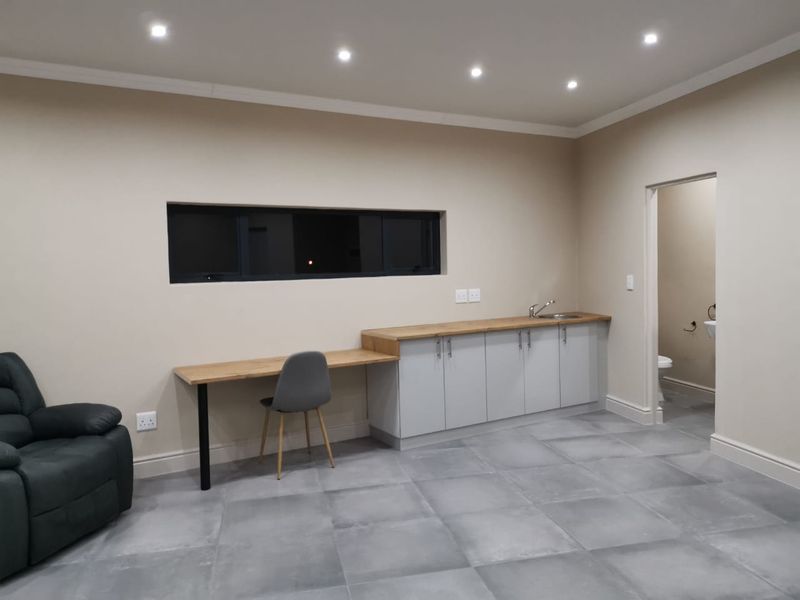 A functional utility space featuring built-in cabinetry with a wooden countertop, integrated sink, tiled flooring, and recessed downlighting, with an adjacent bathroom access.