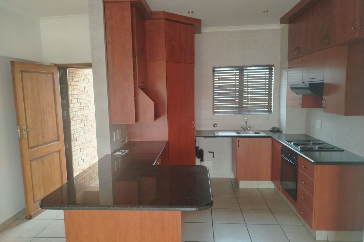 A functional kitchen featuring wooden cabinetry, granite countertops, built-in oven and hob, and tiled flooring, offering a clean and practical workspace.