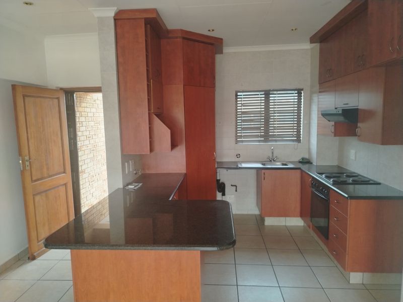 A functional kitchen featuring wooden cabinetry, granite countertops, built-in oven and hob, and tiled flooring, offering a clean and practical workspace.