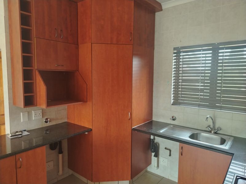 A functional kitchen area featuring wood-look laminate cabinetry, granite countertops, and a stainless steel sink with tiled backsplash.