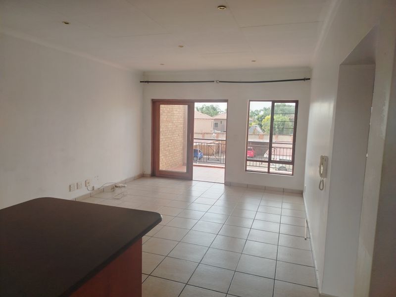 An empty open-plan living area featuring tiled floors, recessed lighting, and a sliding door leading to a balcony.