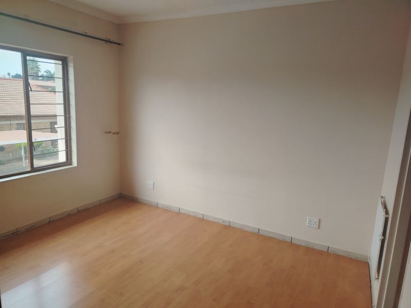 An empty bedroom featuring laminate flooring, a window with security bars, and neutral wall finishes, ready for personalization.