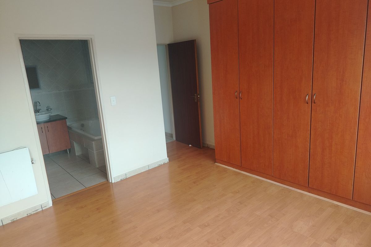 A spacious bedroom featuring built-in wooden cupboards, laminate flooring, and direct access to an en-suite bathroom.