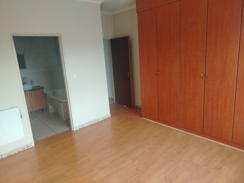 A spacious bedroom featuring built-in wooden cupboards, laminate flooring, and direct access to an en-suite bathroom.