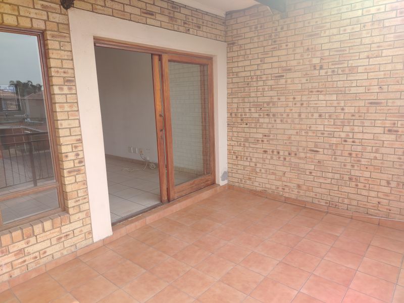 A covered patio area featuring exposed brick walls, tiled flooring, and a sliding glass door providing access to the interior living space.