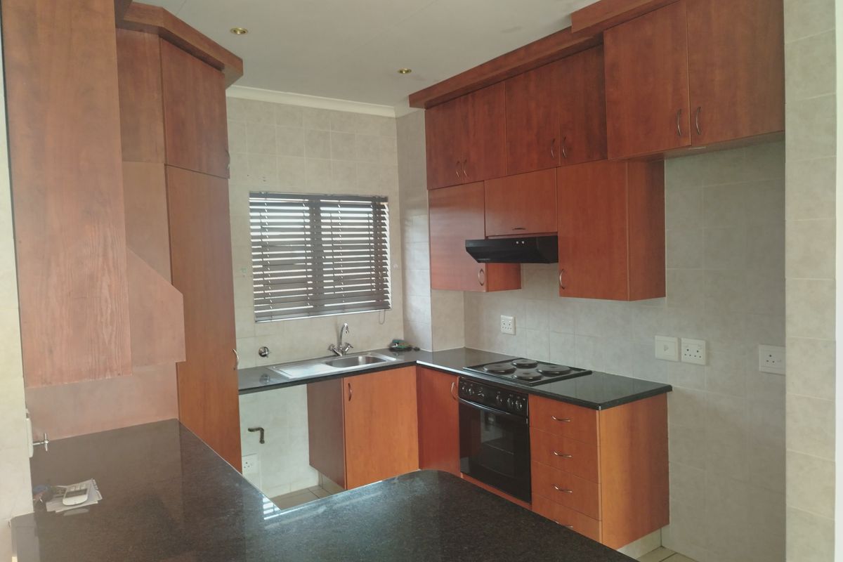 A functional kitchen featuring wooden cabinetry, granite countertops, a built-in oven, electric hob, and an extractor fan, offering a clean and practical workspace.