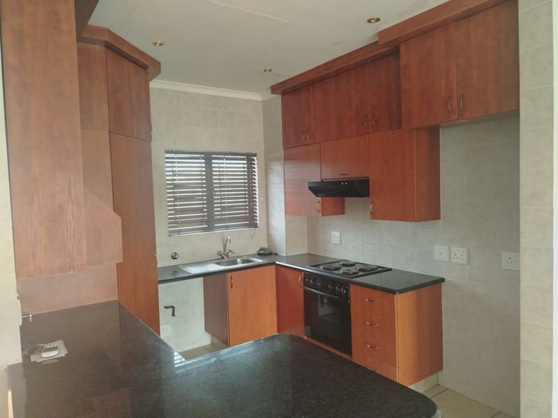 A functional kitchen featuring wooden cabinetry, granite countertops, a built-in oven, electric hob, and an extractor fan, offering a clean and practical workspace.